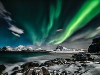 Bright green and blue northern lights above a Norwegian fjord and mountain range