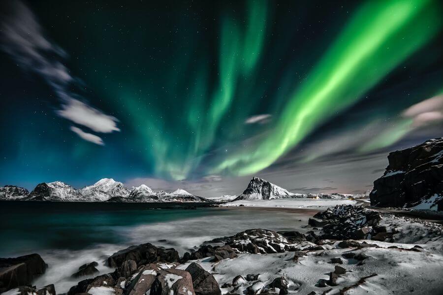 Bright green and blue northern lights above a Norwegian fjord and mountain range