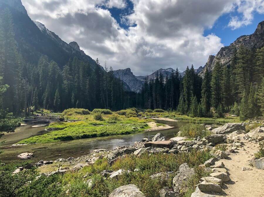 A river with grassy banks winding through multiple mountain peaks in the Grand Tetons