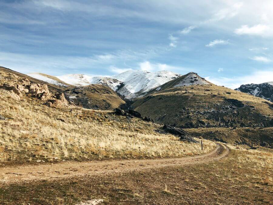 A trail on Antelope Island, Utah leading up a grassy mountain whose top is covered in snow