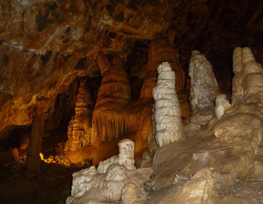 The dark inside of a cave with stalagmites and stalactites illuminated by an orange glow