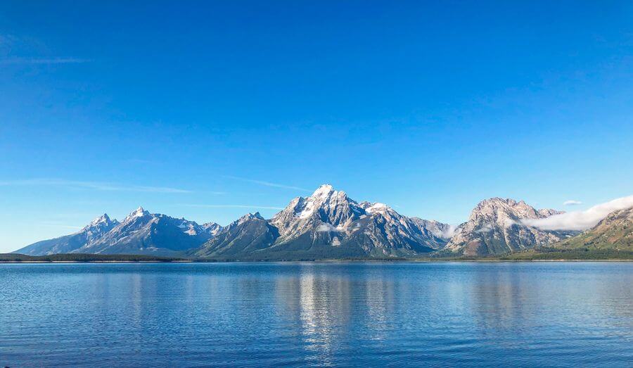 A panoramic view of the Teton mountain range on a cloudless day with Jackson Lake in the foreground