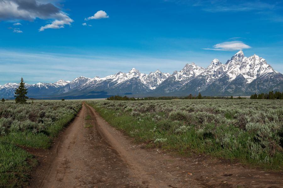 A stunning view of the snow capped Grand Teton mountains as seen from a dirt road