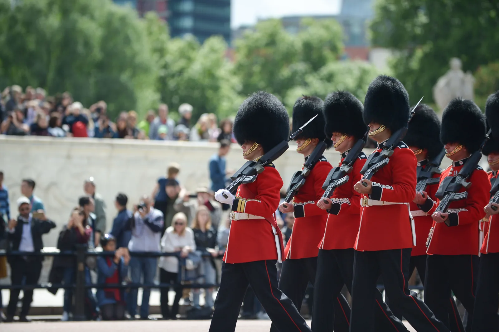Guards in red tunics marching past a crowd of onlookers