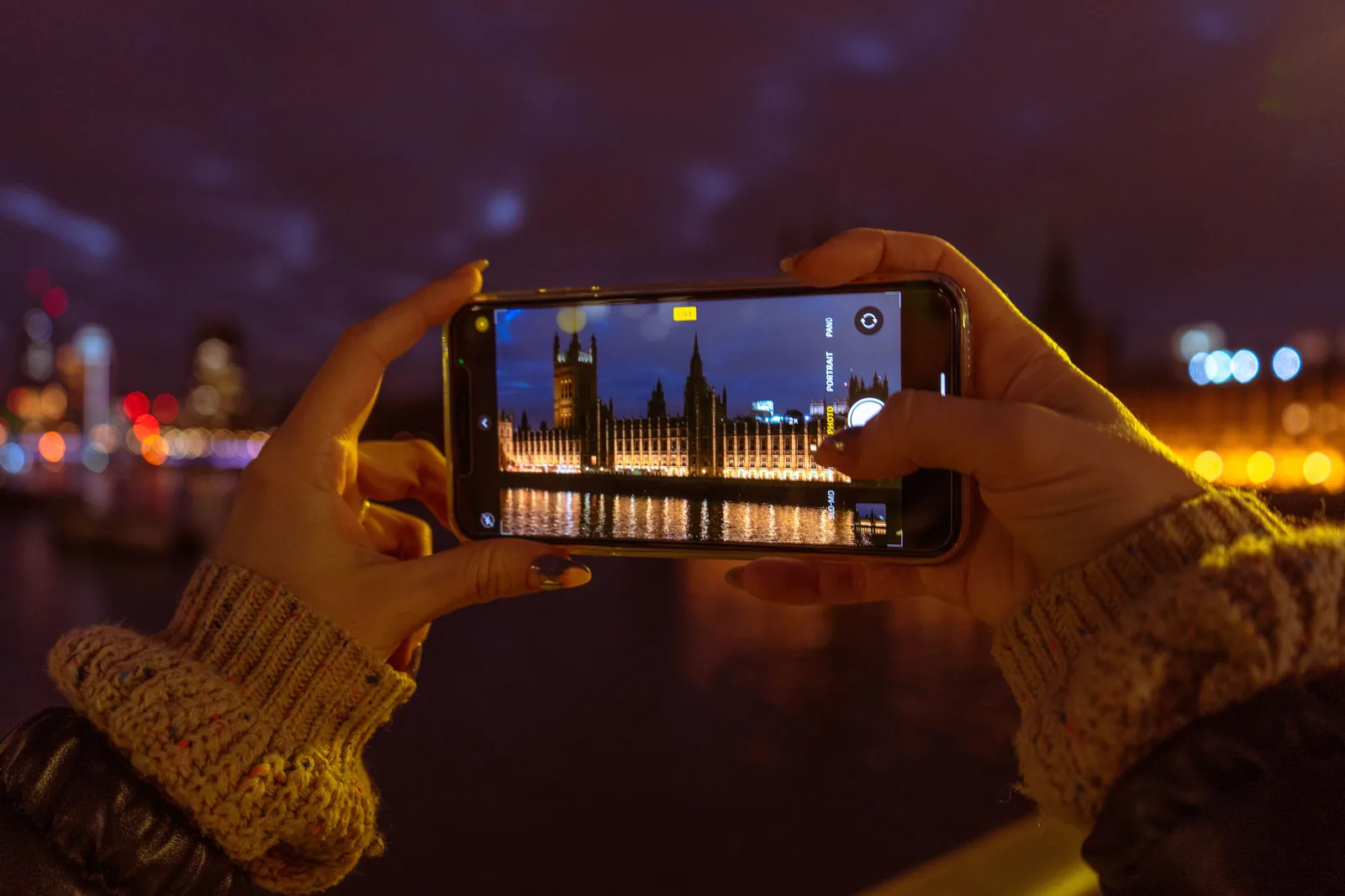 Someone photographing the London skyline with a smartphone at dusk