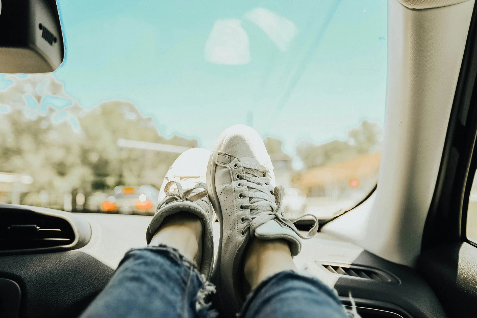 A passenger's sneakers propped up on the dashboard on a sunny road trip