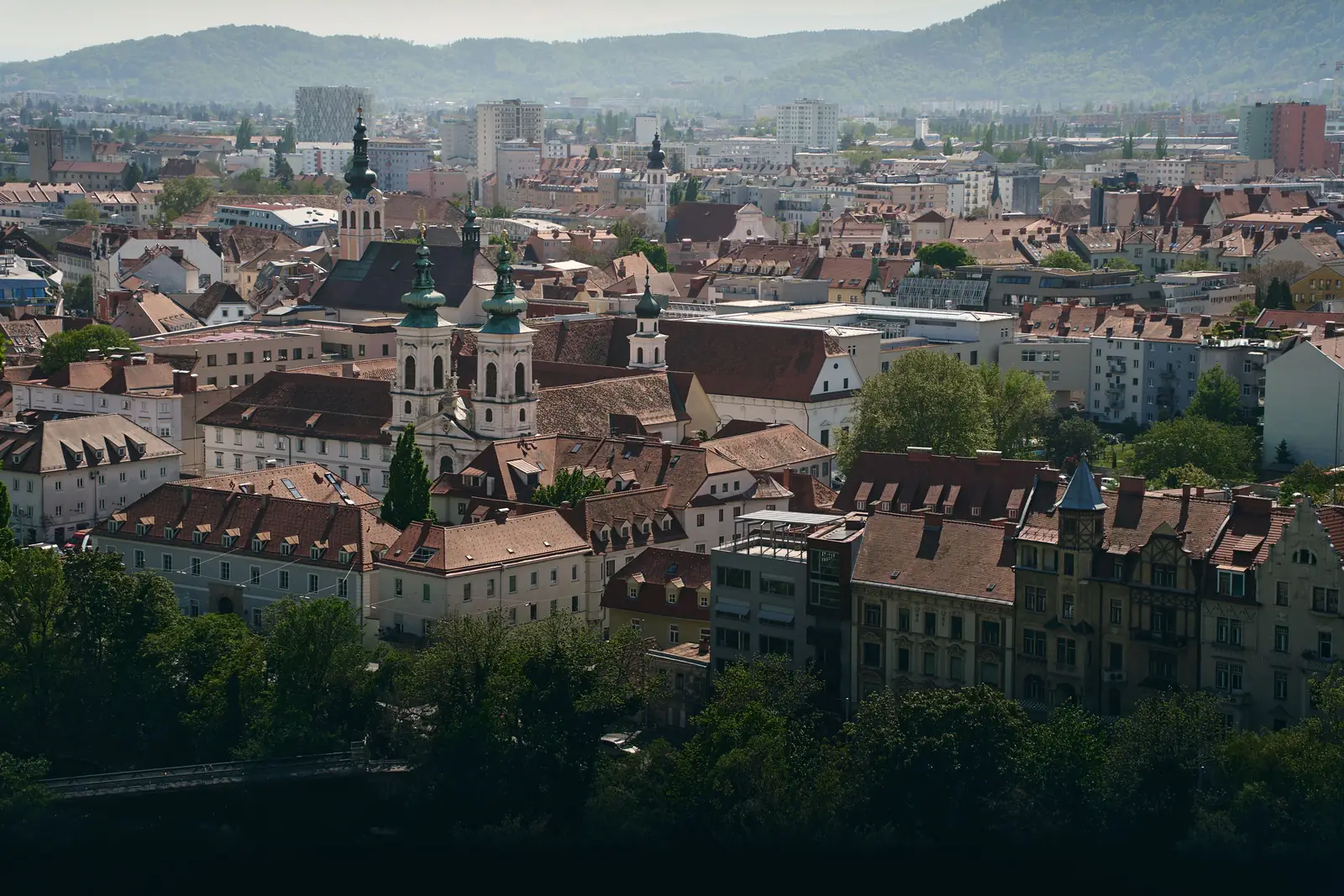 View across the rooftops and church towers of Graz, Austria, with green hills behind the city
