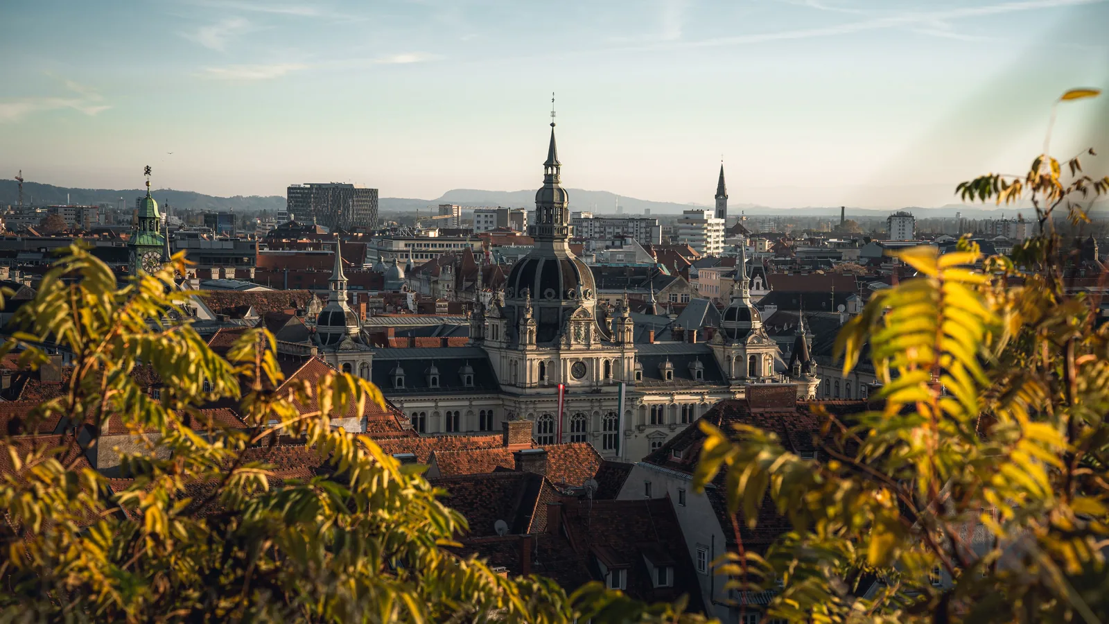 Golden evening light over the domes, spires, and red rooftops of Graz, Austria