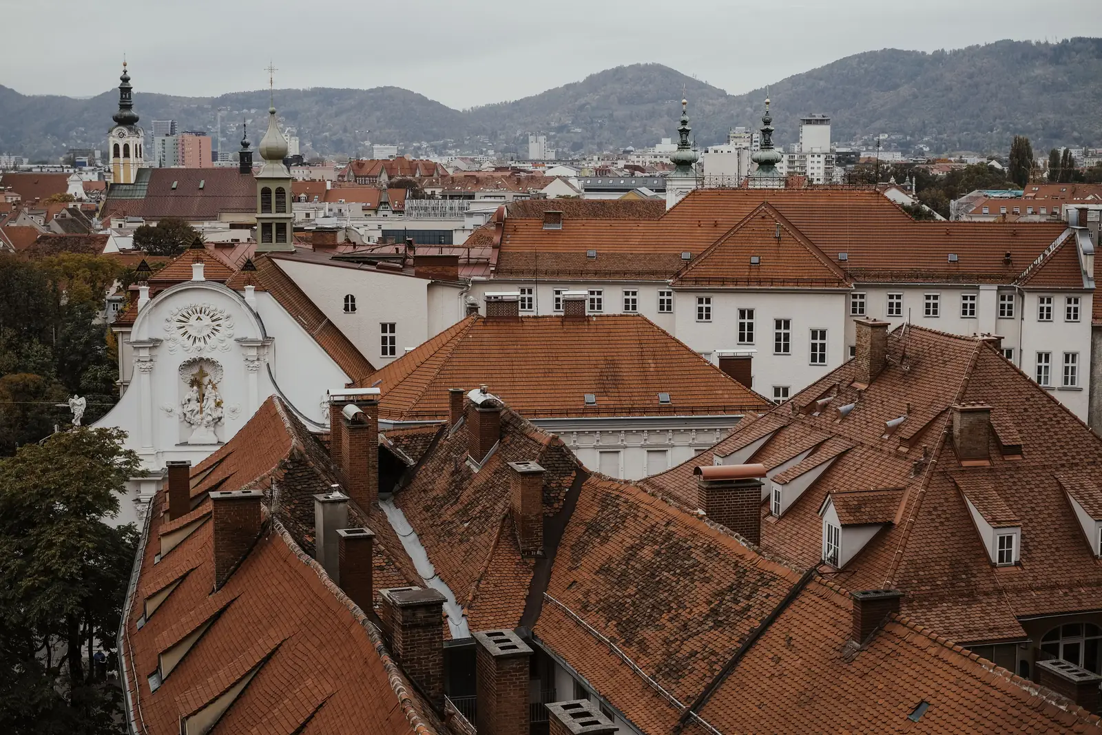 Red tile rooftops and church spires of the Graz old town seen from Schlossberg with hills behind