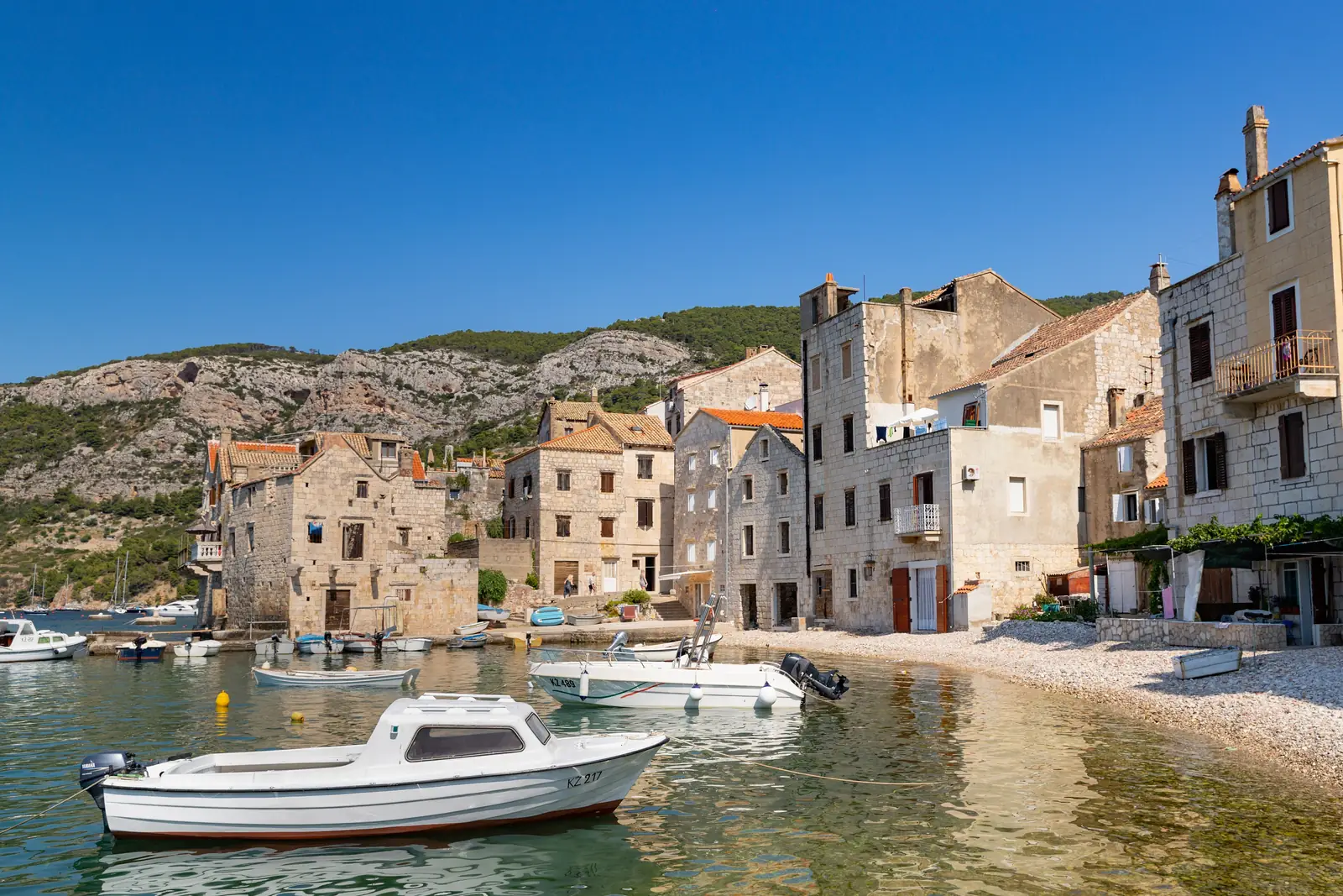 Fishing boats moored in front of stone houses in Komiza harbor on Vis, Croatia