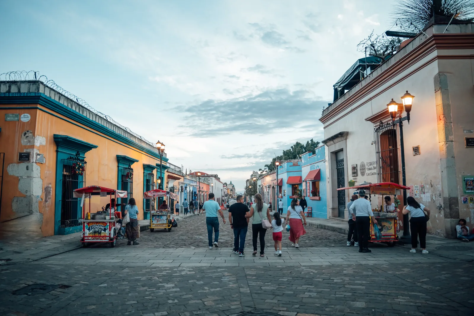 People walking past colorful buildings in Oaxaca city at dusk
