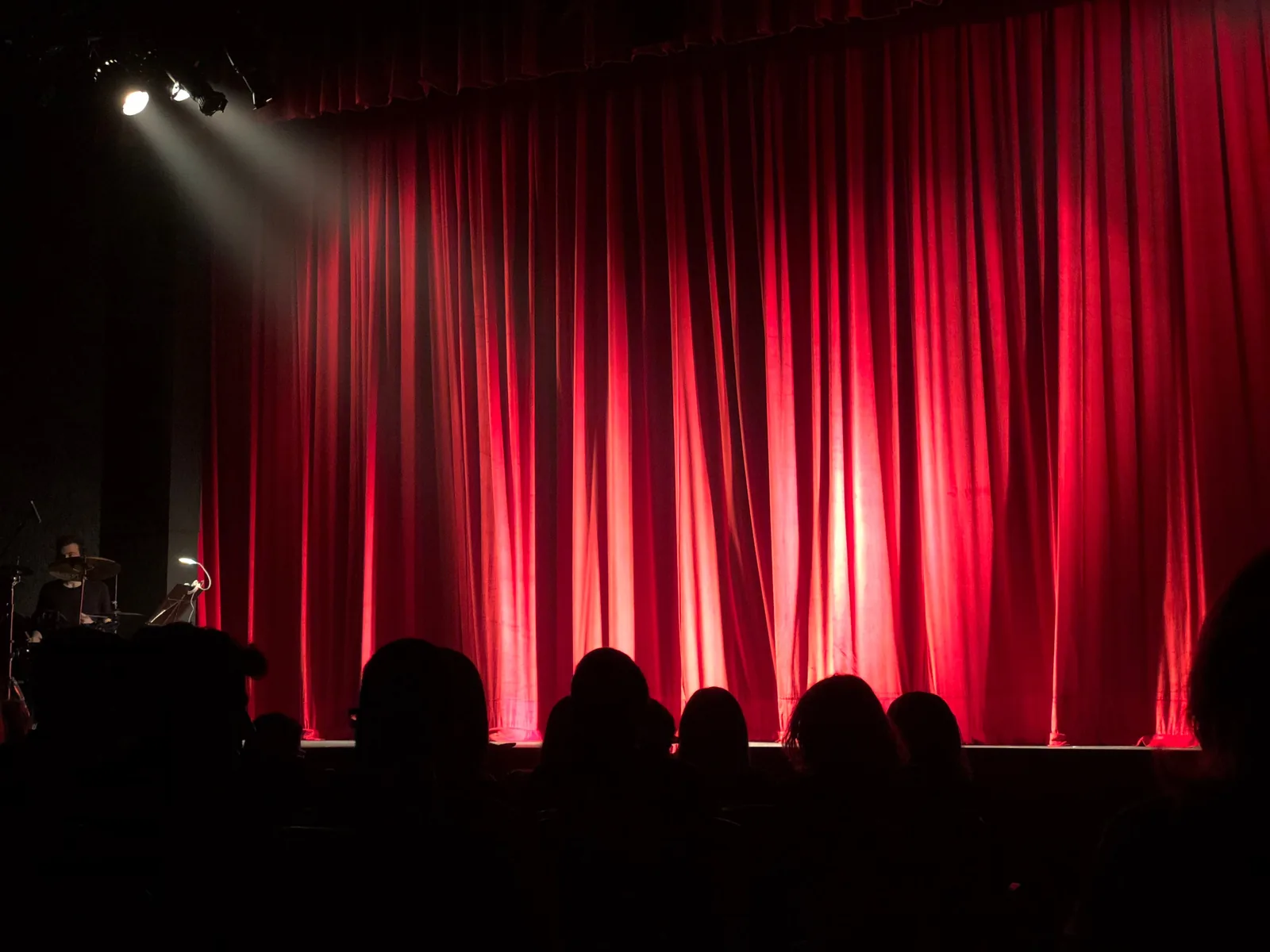 A theater stage lit behind a red curtain before a live show