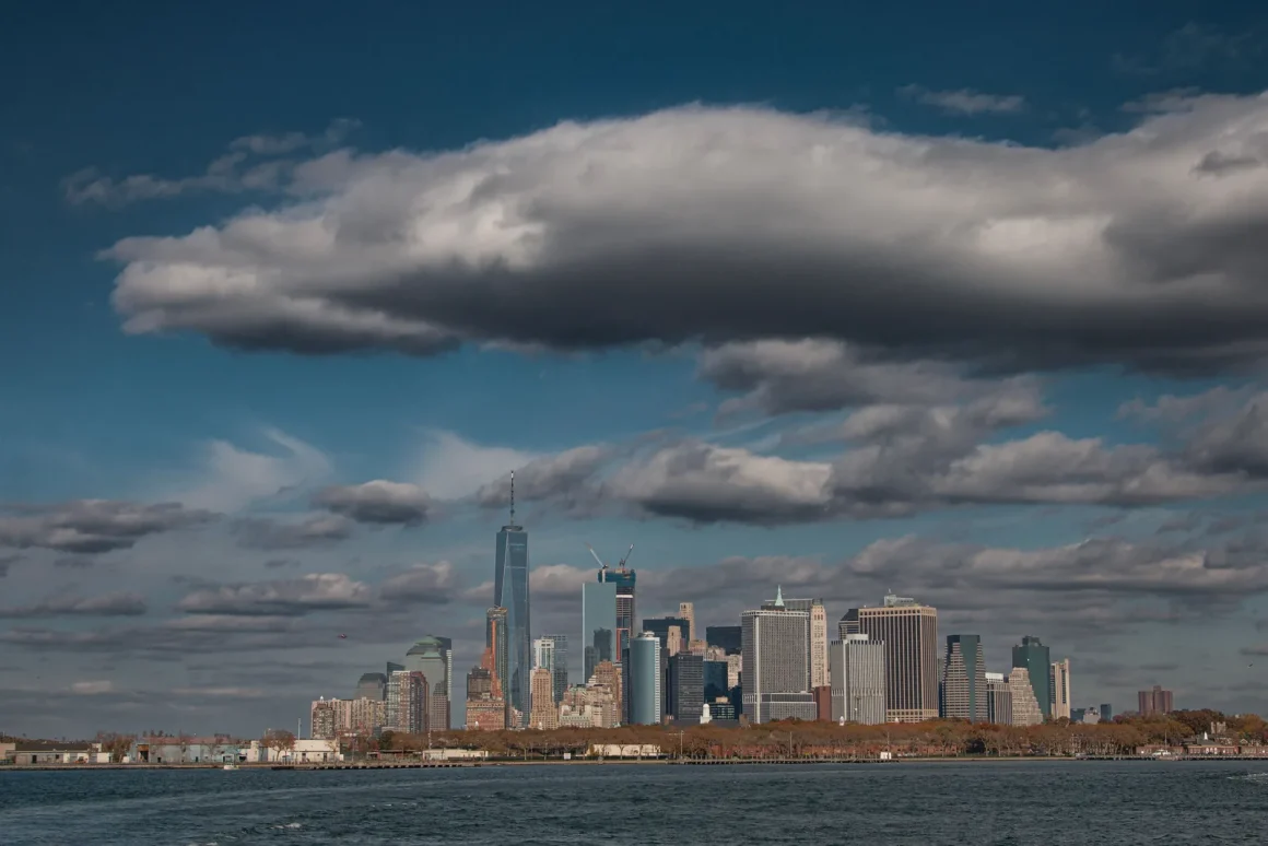 Lower Manhattan skyline seen across the harbor under dramatic clouds