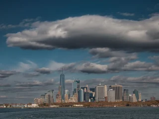 Lower Manhattan skyline seen across the harbor under dramatic clouds