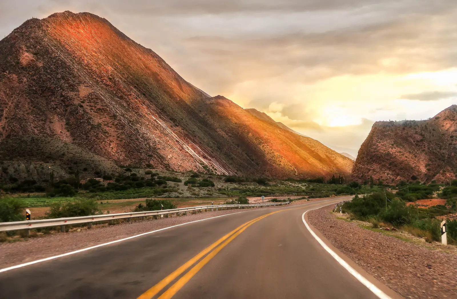 An open road curving toward a mountain lit by golden sunset light