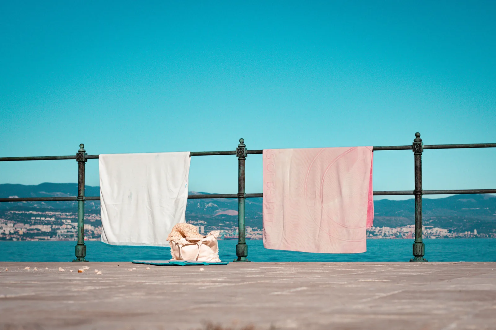 Beach towels drying on a railing above the sea