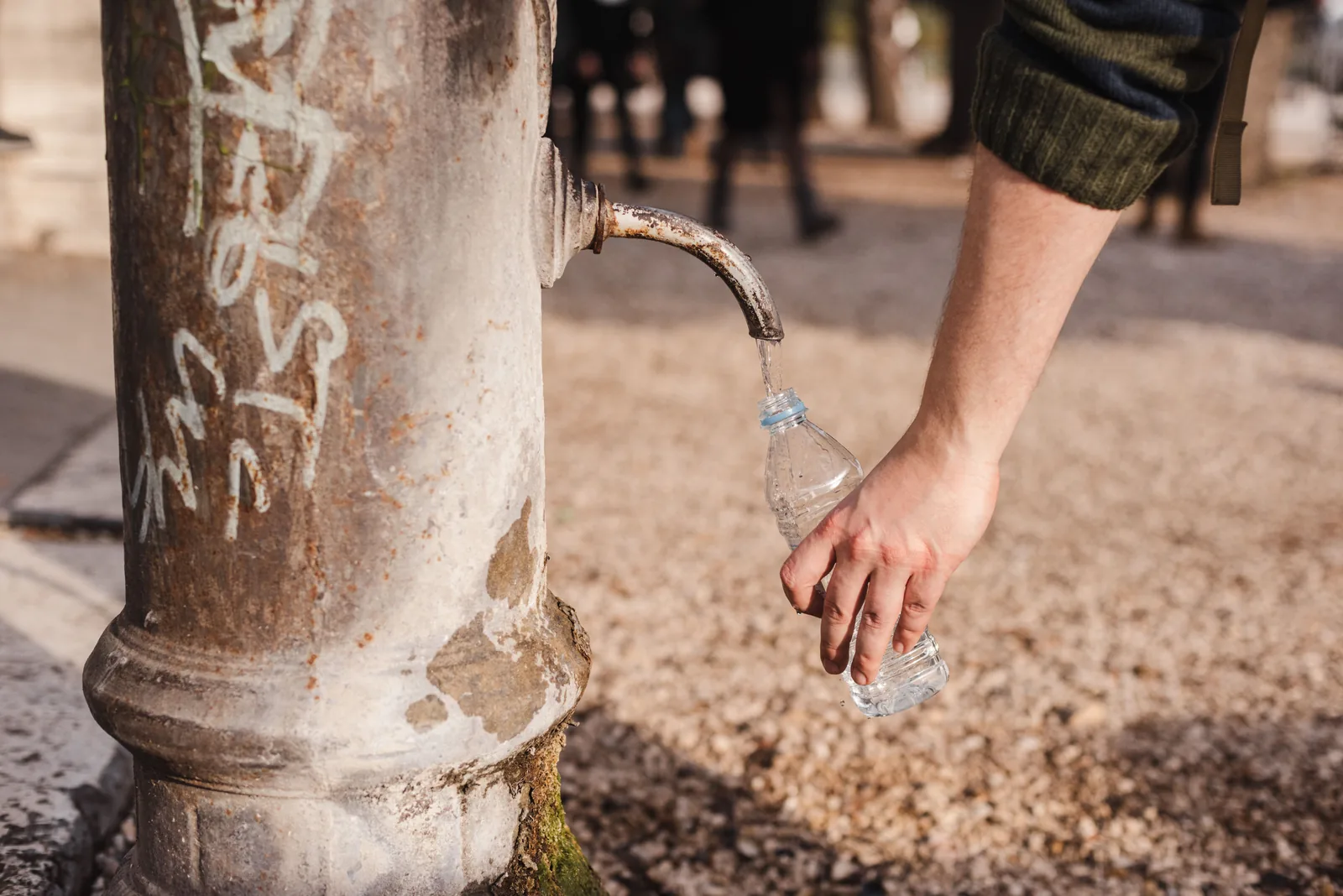 A hand filling a bottle from one of the cast iron street fountains in Rome