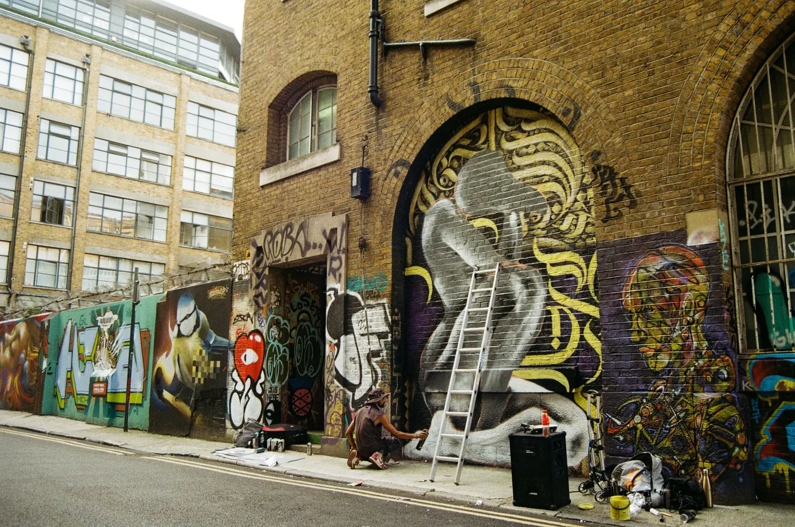 An artist on a ladder painting a mural on a Shoreditch wall