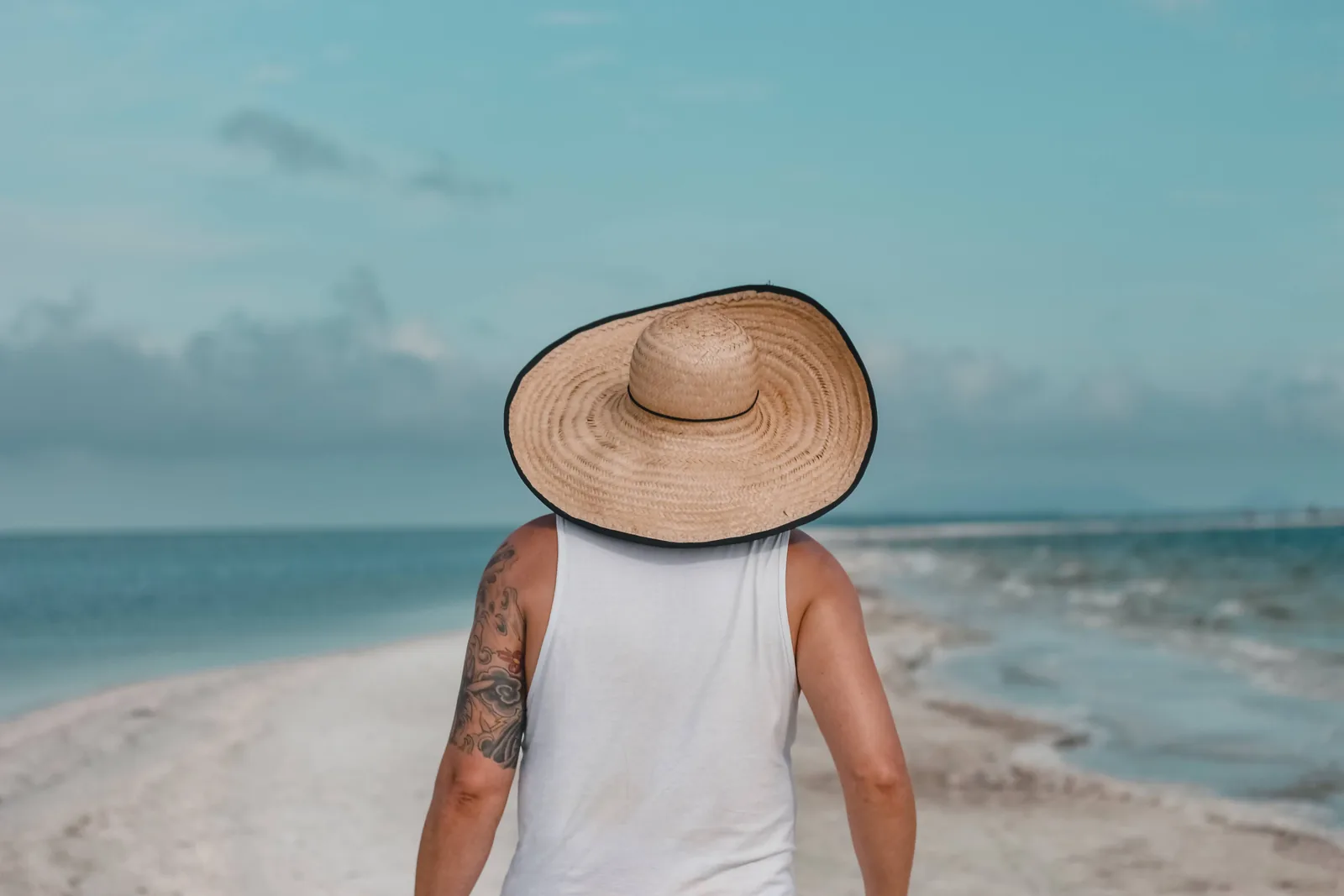 A person in a wide brimmed straw hat standing on a sunny beach