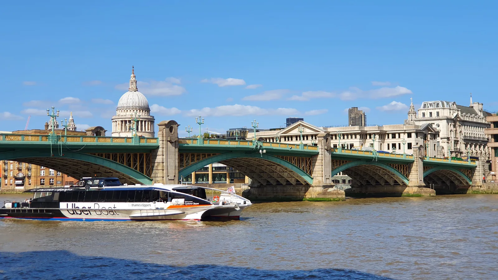 A Thames Clippers boat passing under a bridge with St Paul's behind