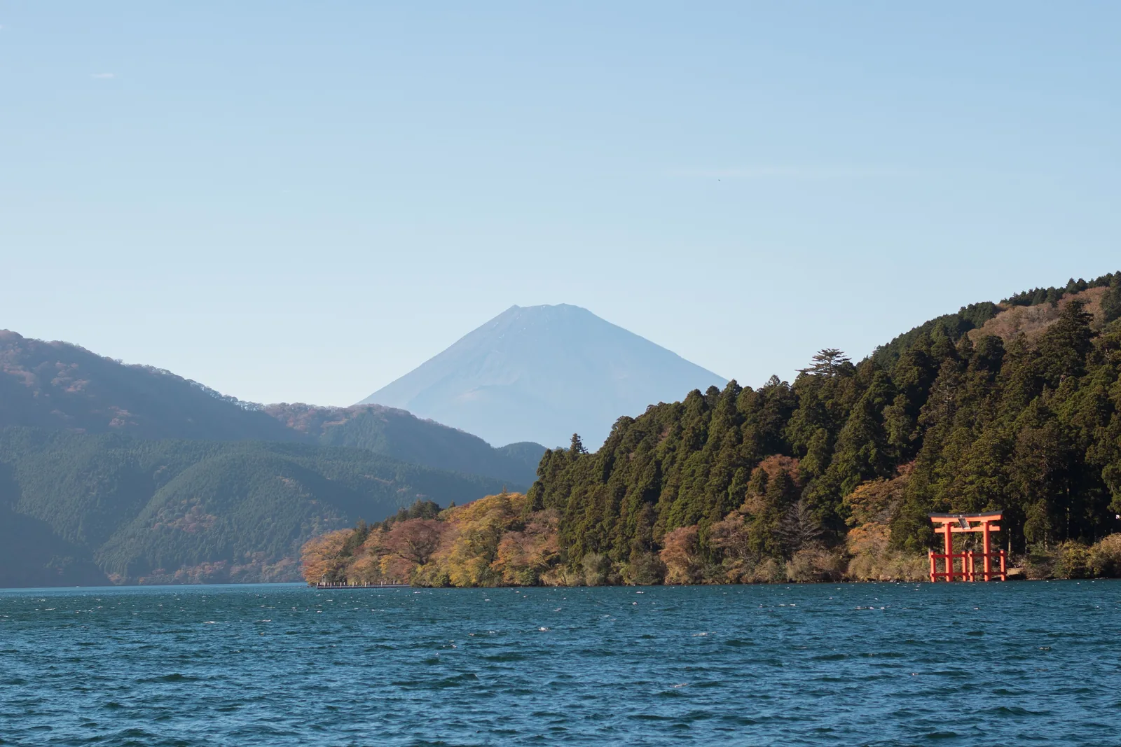 A red torii gate on the shore of Lake Ashi in Hakone with Mount Fuji behind it