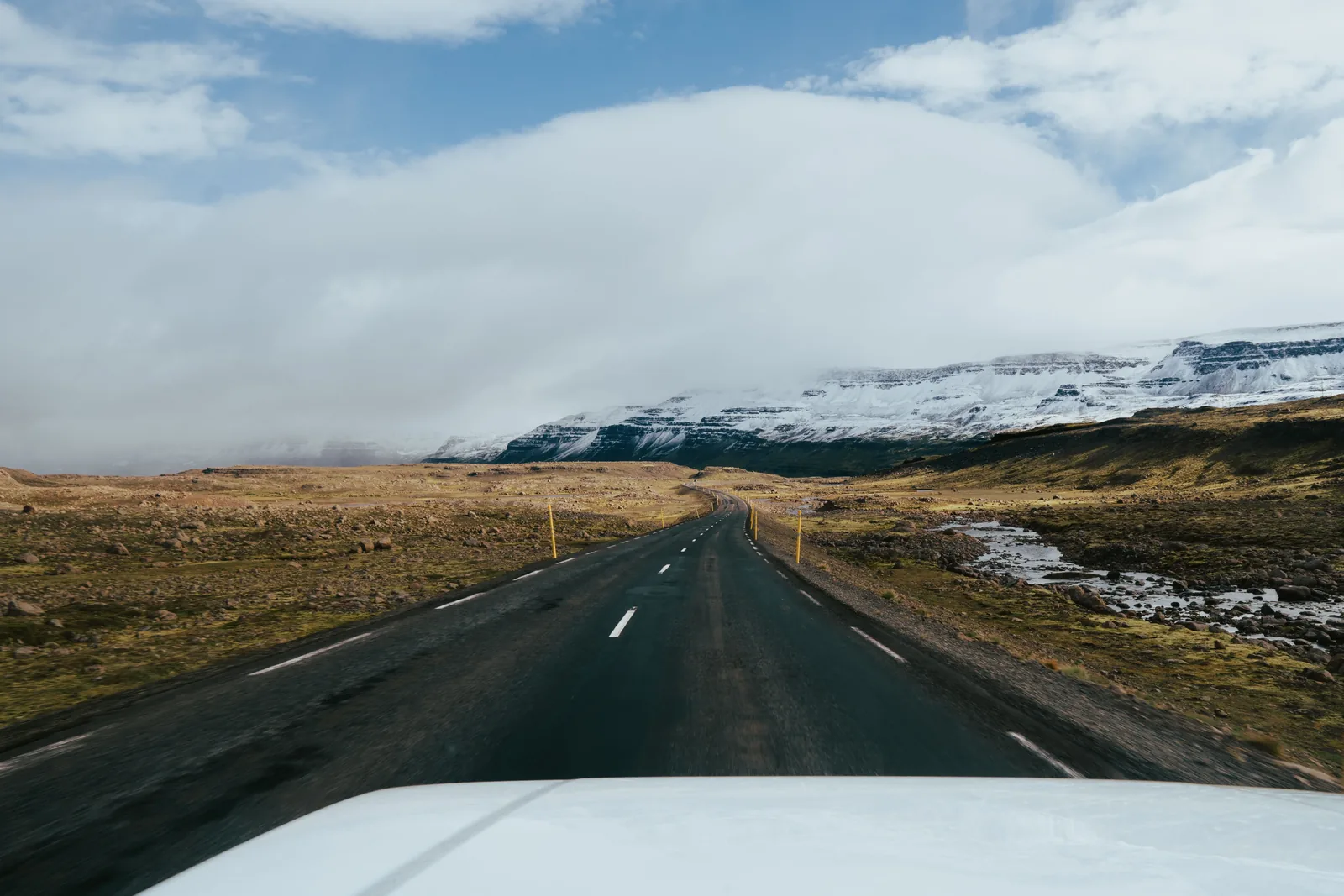 The view down an empty Icelandic road toward a snow covered ridge from inside a car