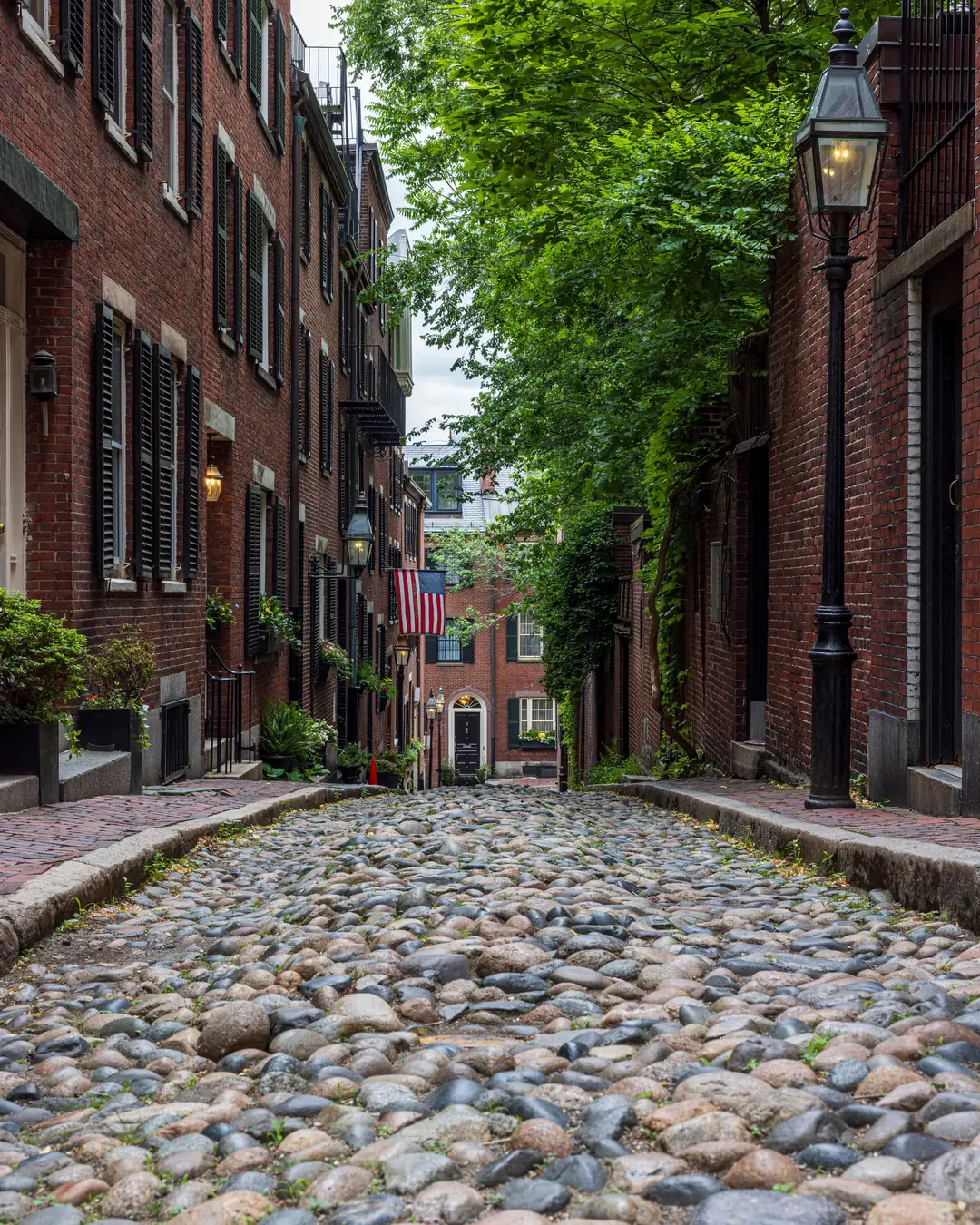 A narrow cobblestone lane lined with brick row houses and a gas lamp in Beacon Hill