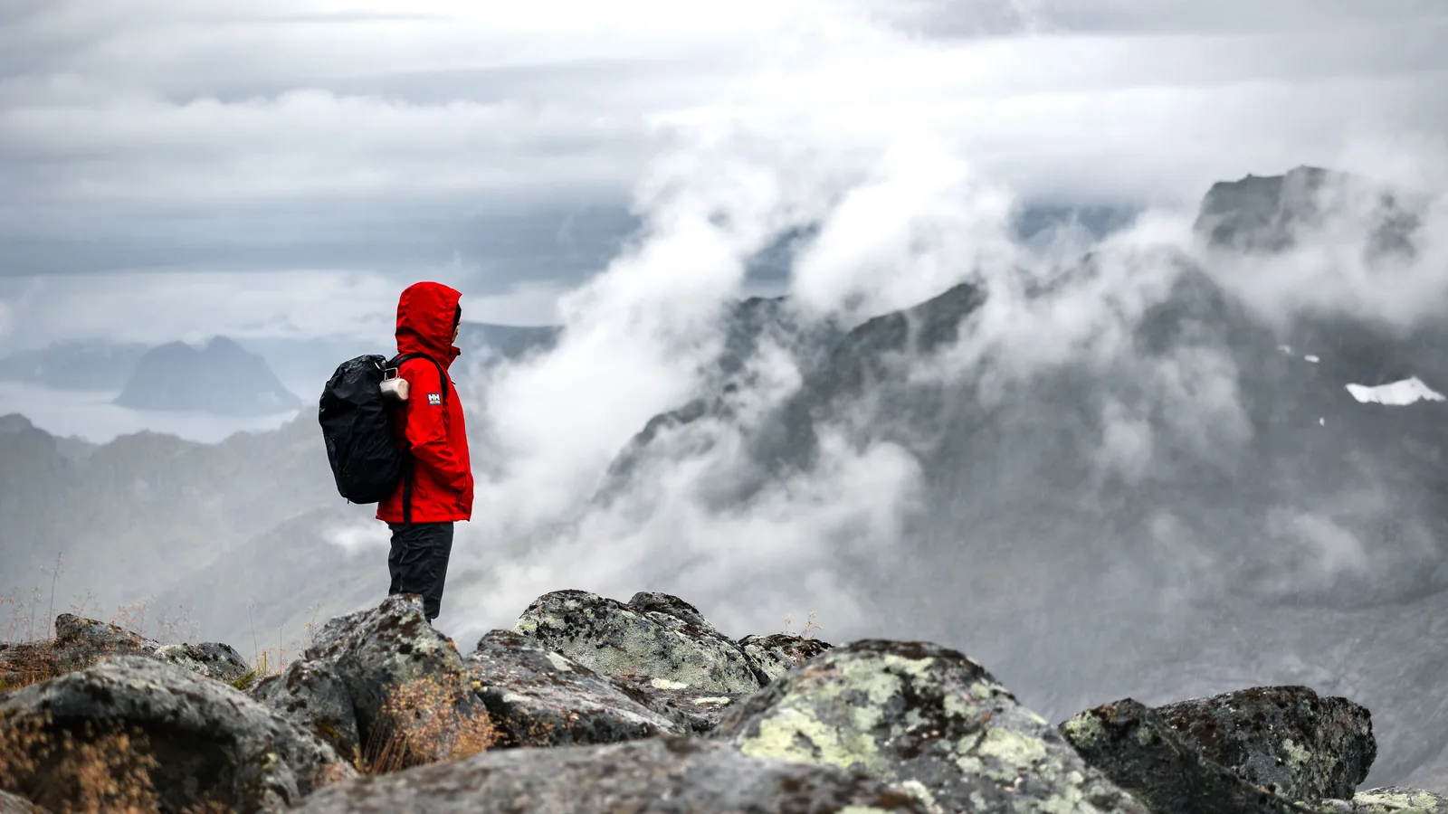 A hiker in a red jacket standing above the clouds on a cold ridge