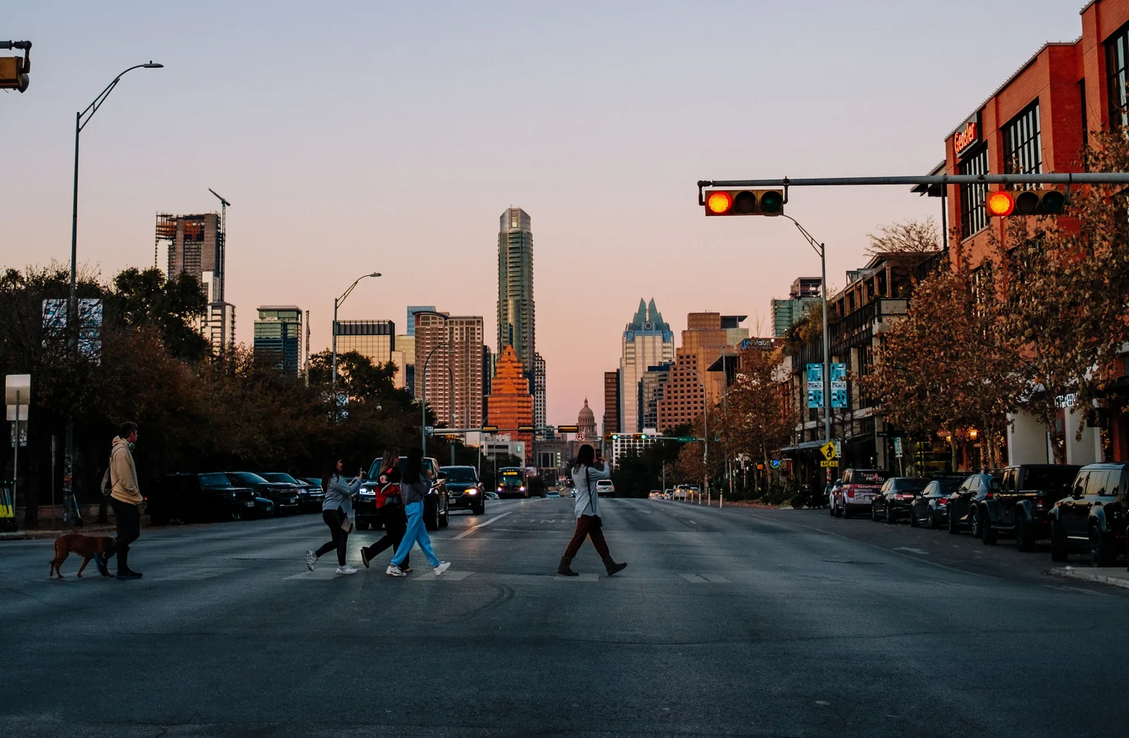 People crossing the street with the downtown Austin skyline behind them at dusk