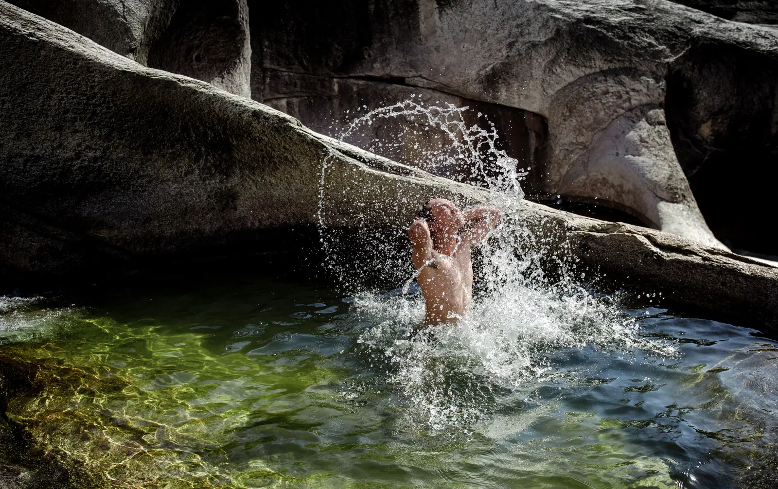 A swimmer jumping into a green pool below a limestone overhang