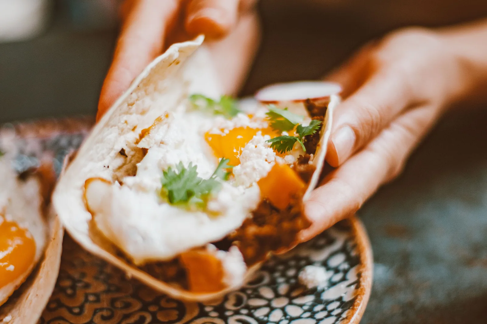 Hands holding a breakfast taco with a fried egg