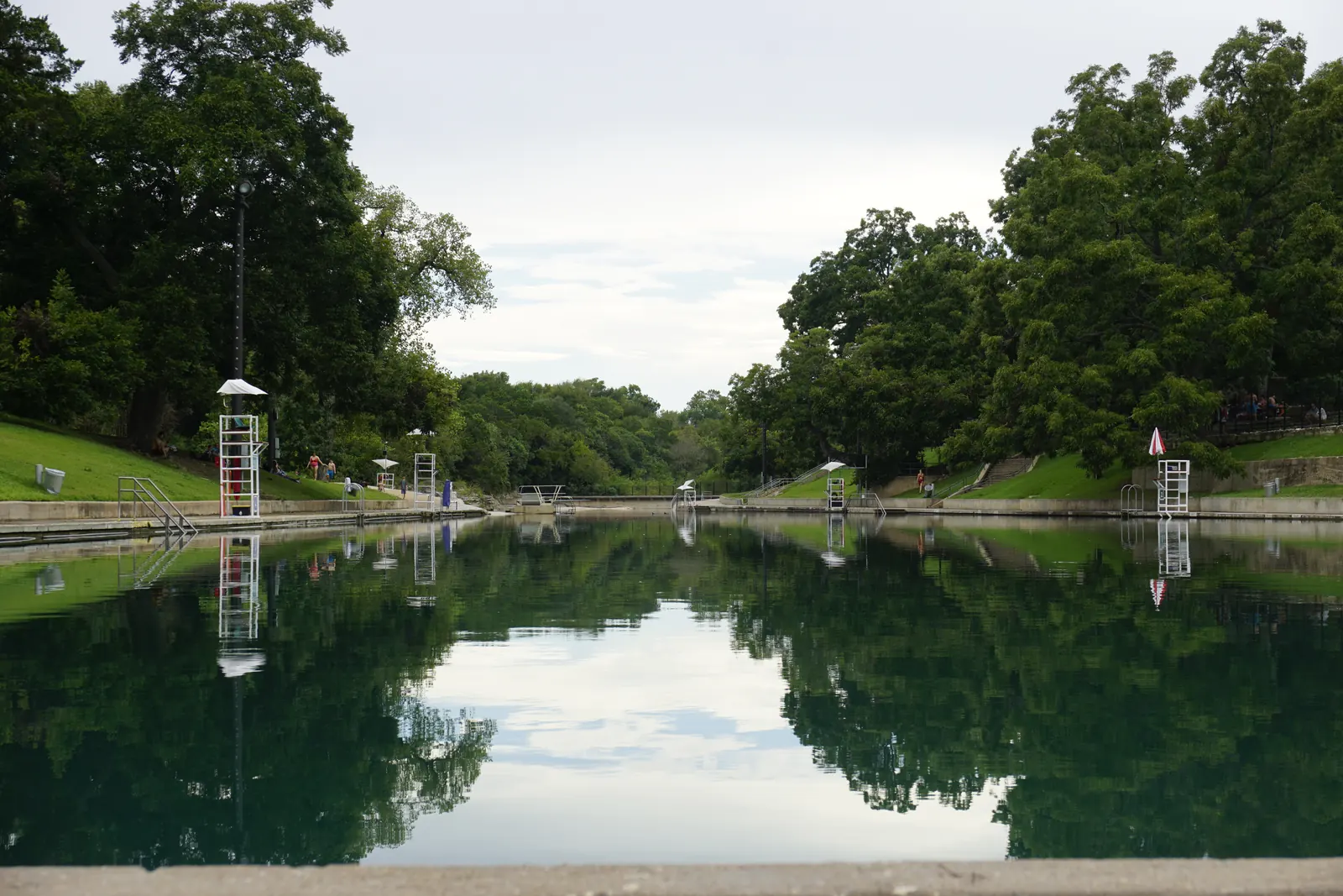 The long spring fed channel of Barton Springs Pool reflecting the trees along its banks