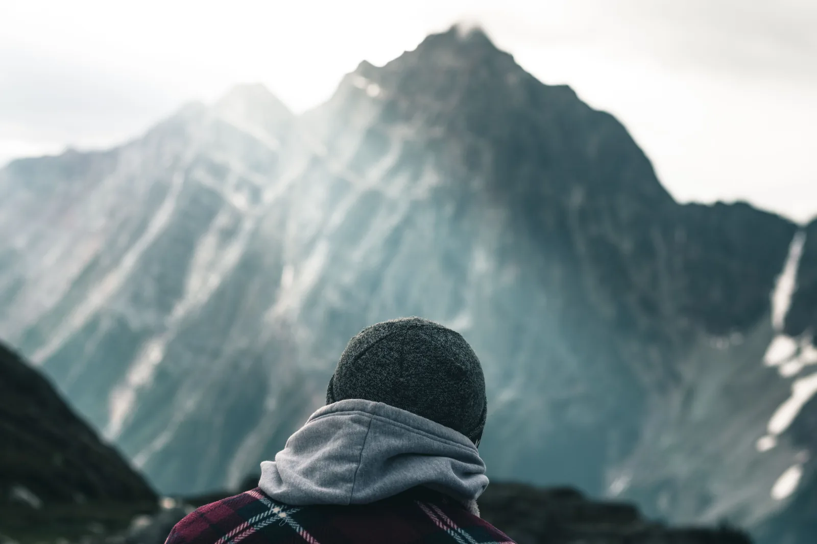 A person in a hood and beanie looking out at snow covered mountains