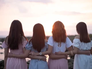 Four friends standing arm in arm watching the sun set over the water