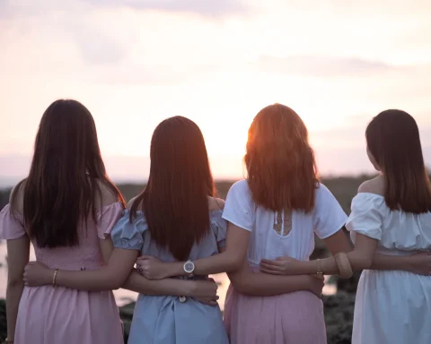 Four friends standing arm in arm watching the sun set over the water