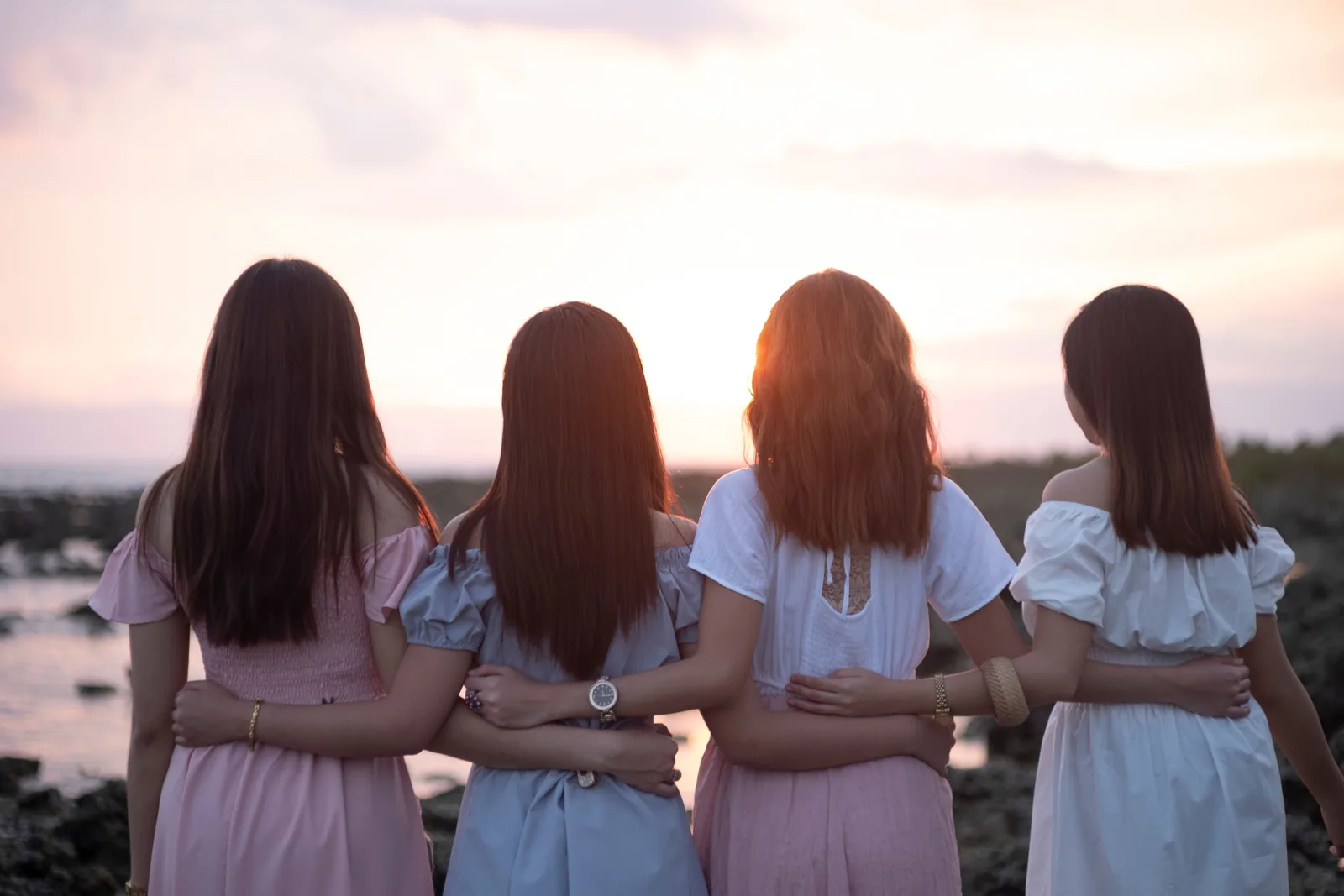 Four friends standing arm in arm watching the sun set over the water