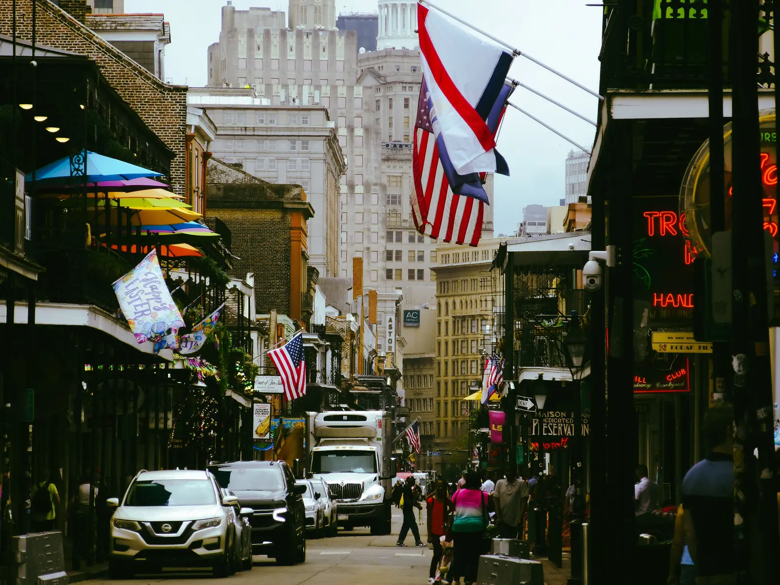 Neon club signs and flags hanging over a busy Bourbon Street in the French Quarter