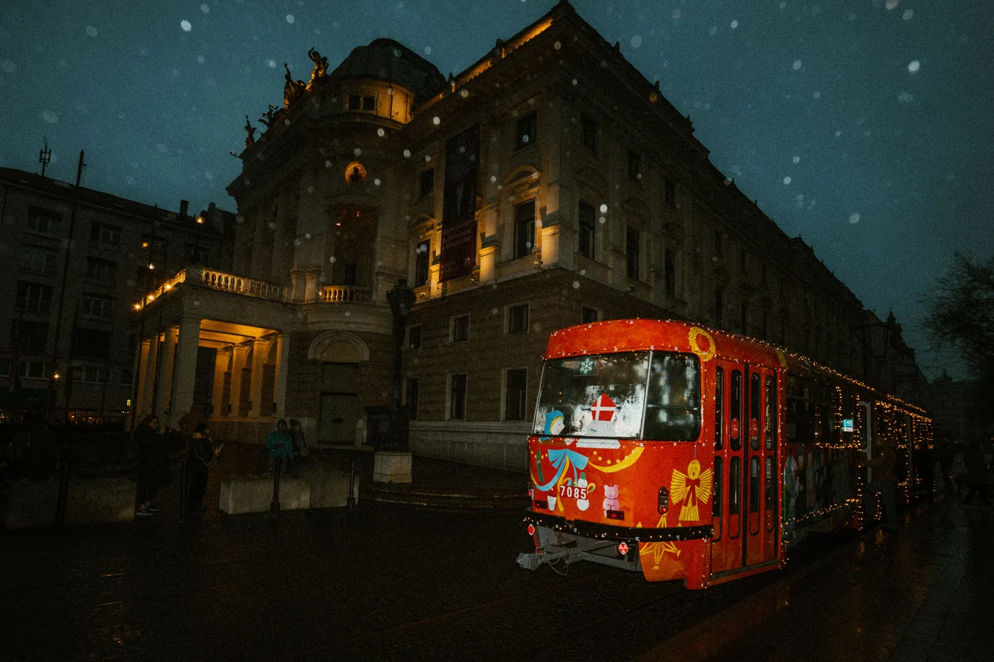 A tram decorated with Christmas lights passing through Budapest in falling snow