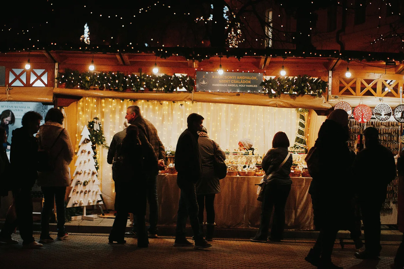 Shoppers browsing a lit Christmas market stall in Budapest after dark