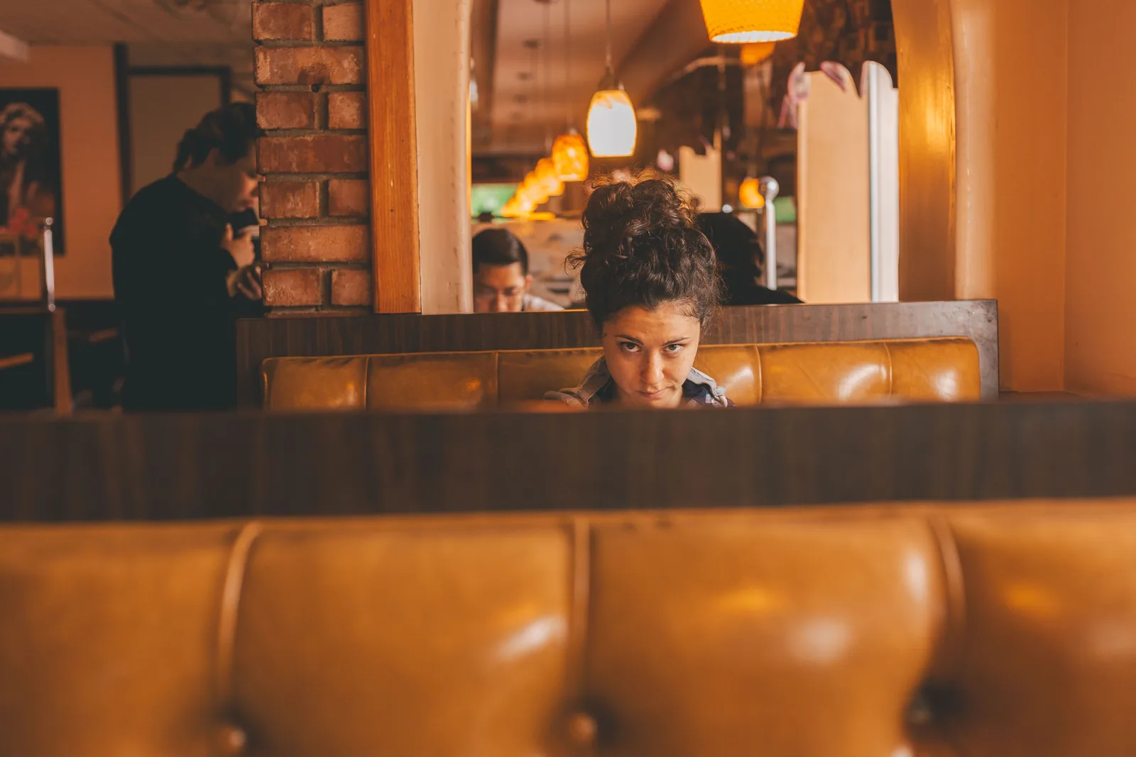 A woman sitting in a restaurant booth in warm light with the bar behind her
