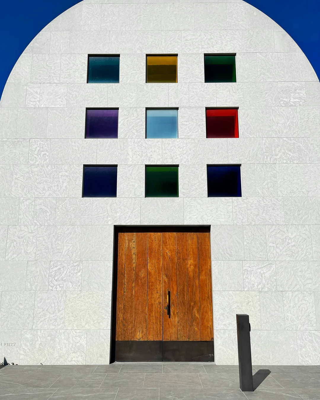A white stone building with an arched roof and nine coloured glass windows above a wooden door