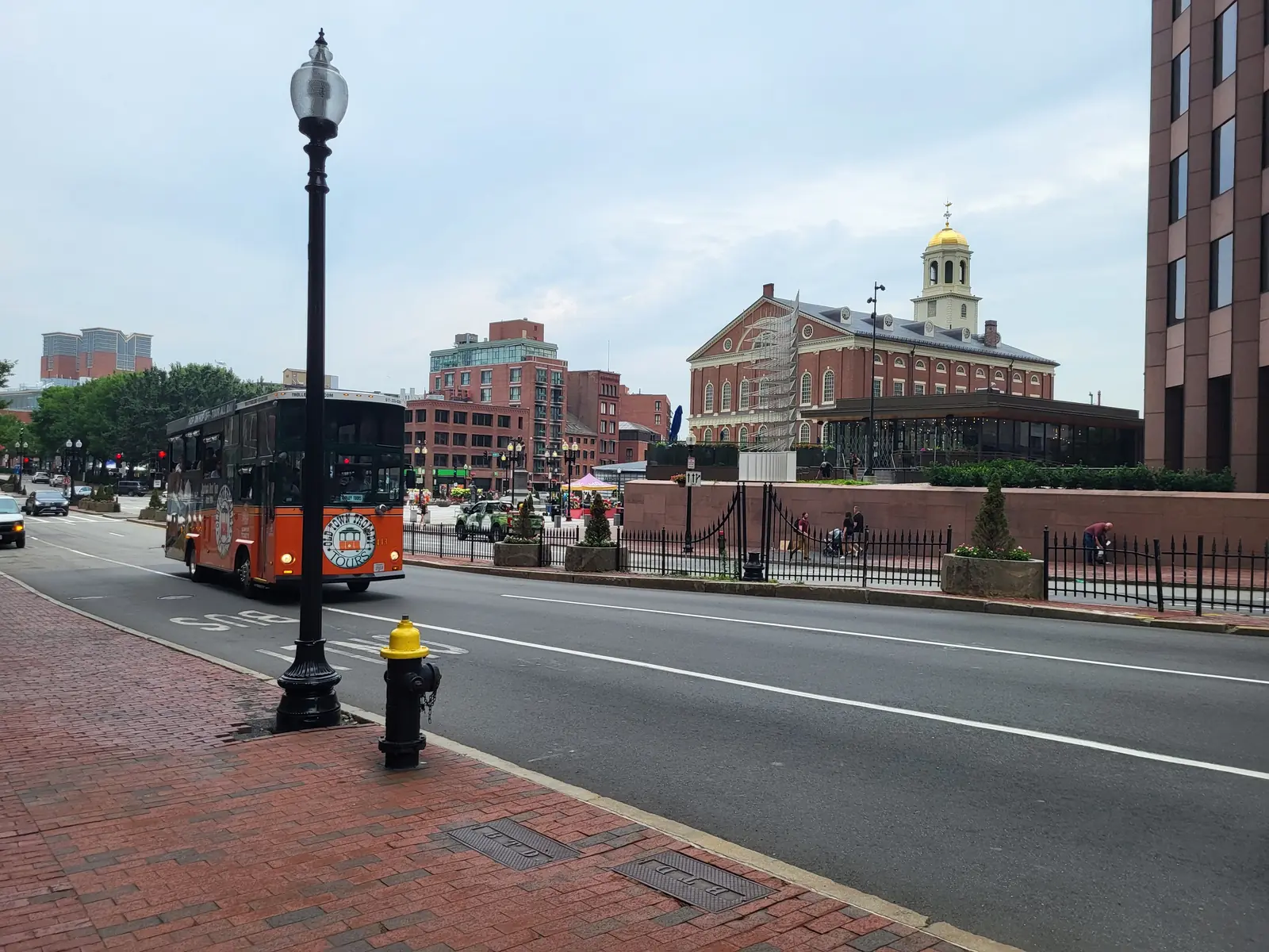 A trolley passing Faneuil Hall on a brick lined street in downtown Boston