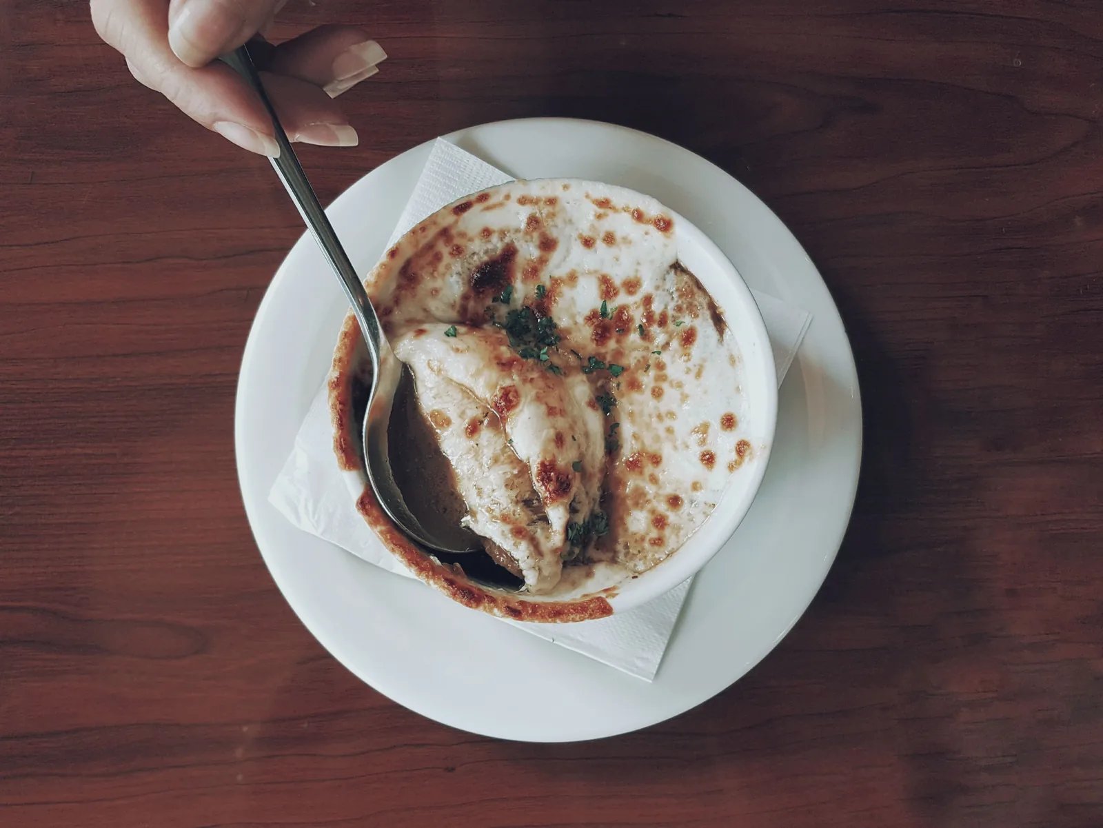 A spoon lifting melted cheese from a bowl of French onion soup