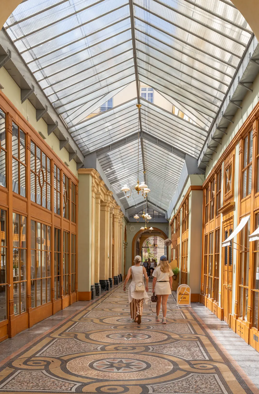 Two people walking through Galerie Vivienne in Paris under its curved glass roof