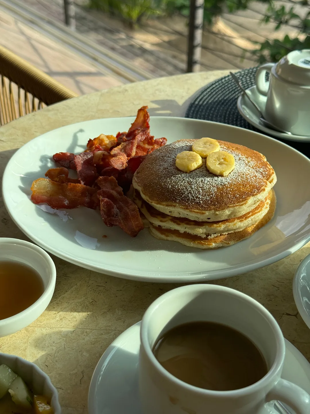 A plate of pancakes with bacon and coffee on a table