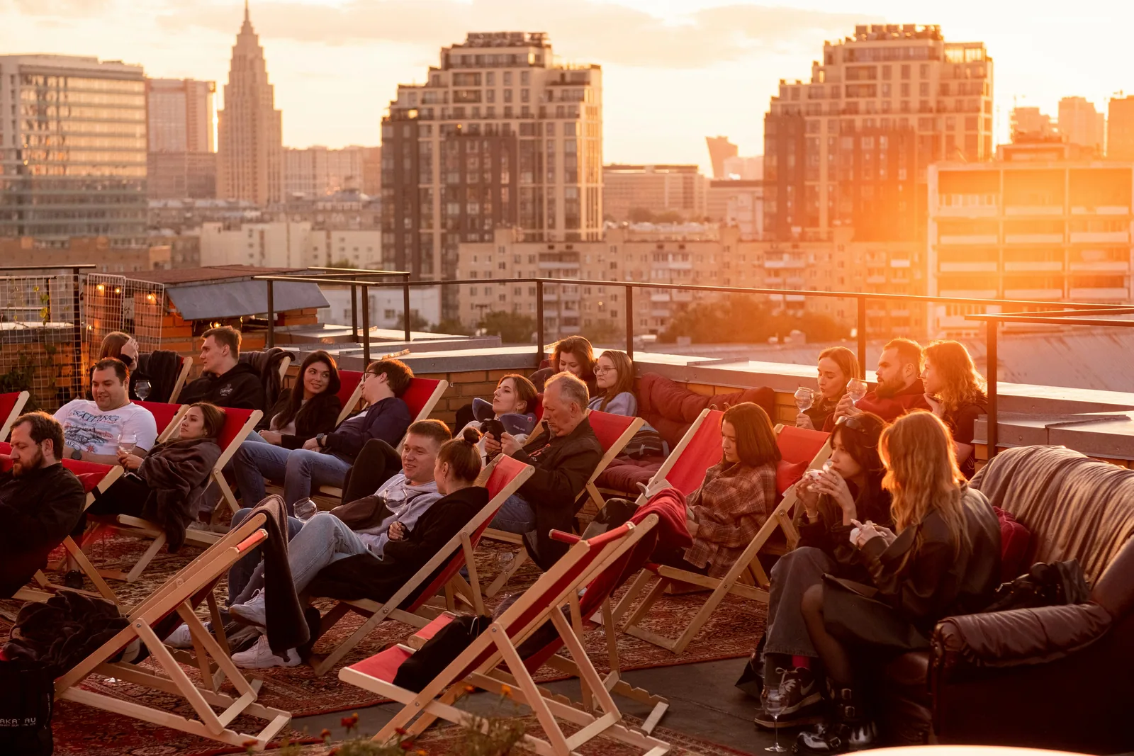 People relaxing in deck chairs on a rooftop terrace at sunset above the city