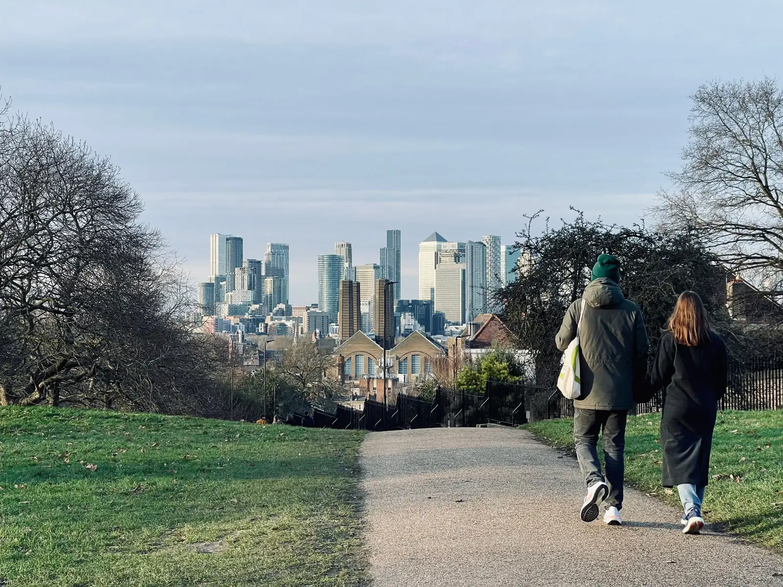 Two people walking in Greenwich Park with the Canary Wharf skyline behind