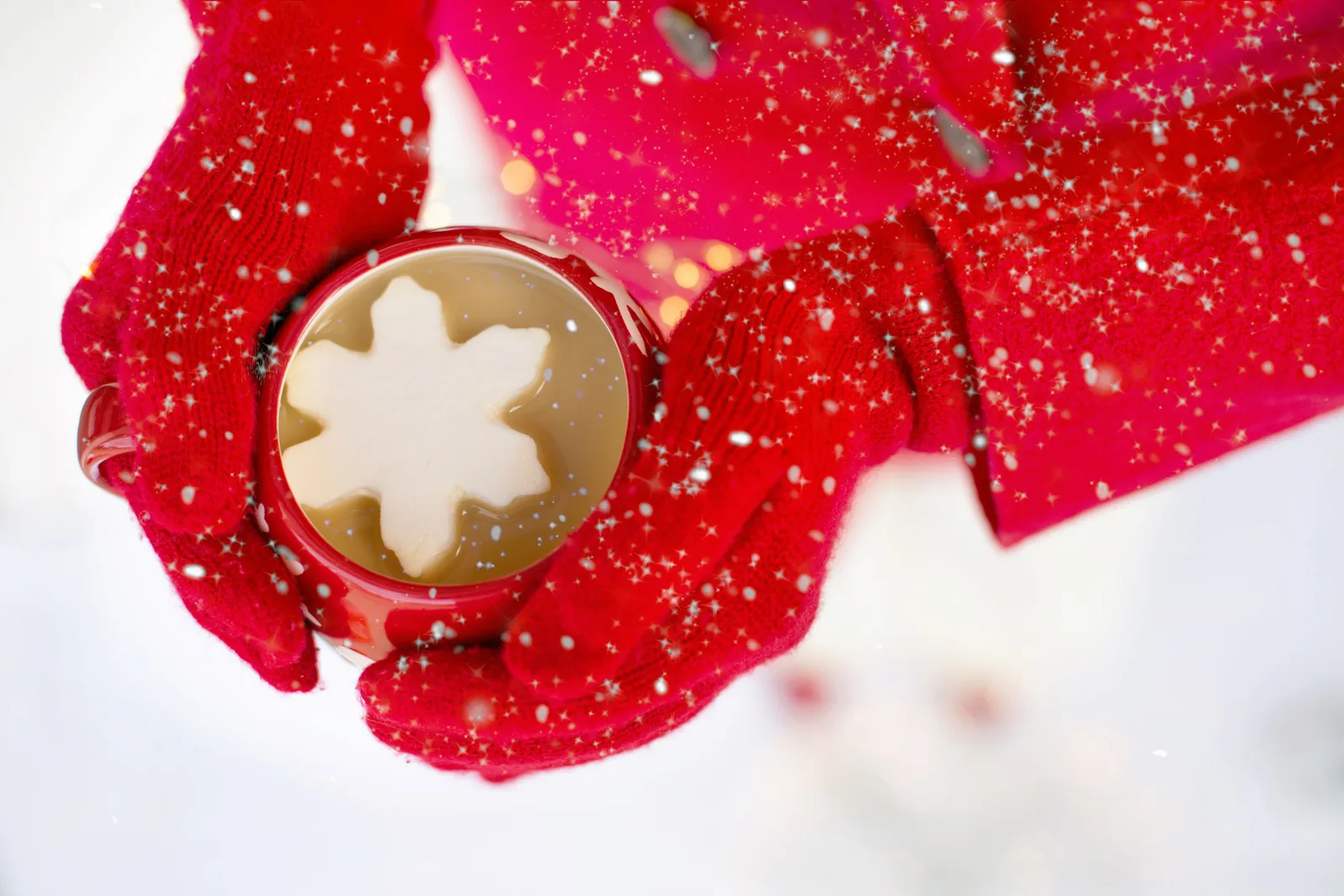 Two hands wrapped around a red mug of hot chocolate