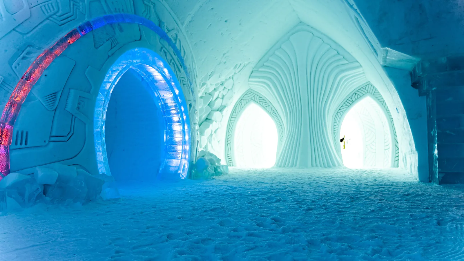 A carved ice corridor lit blue inside an ice hotel