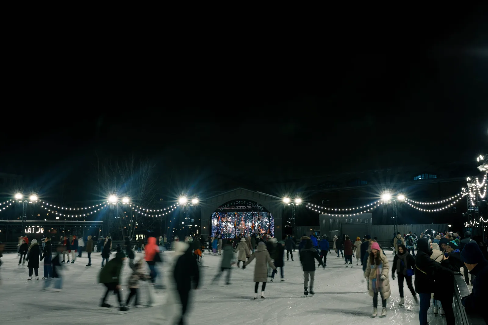 Skaters on an outdoor rink under string lights at night